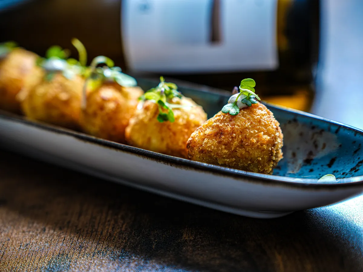 Croquetas caseras servidas en fuente alargada con brotes verdes