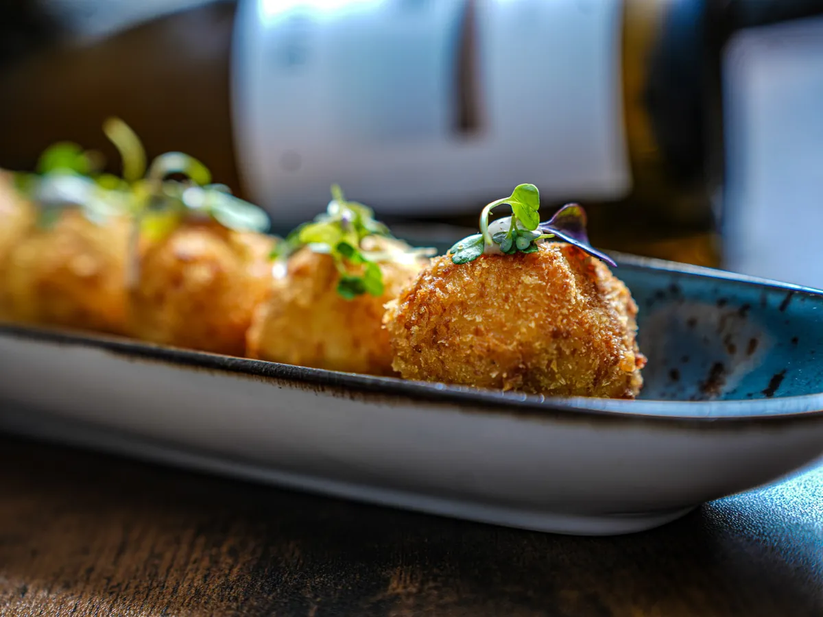 Croquetas caseras con brotes verdes en fuente de cerámica
